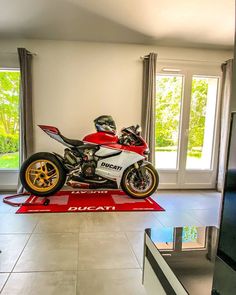 a red and white motorcycle sitting on top of a rug in a living room next to a window