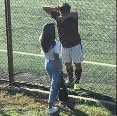 two people standing next to each other near a fence and grass area with a tennis court in the background