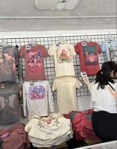 a woman looking at t - shirts on display in a store