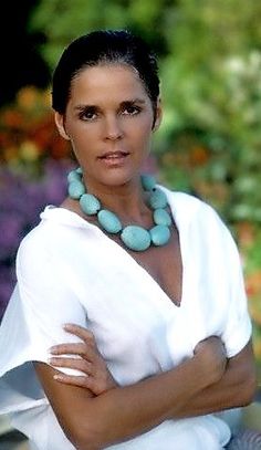 a woman with her arms crossed wearing a white shirt and turquoise necklace on the neck