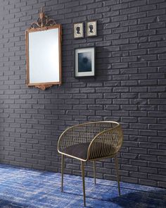 a chair sitting in front of a brick wall next to a mirror and framed pictures