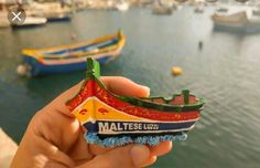 a hand holding a small toy boat in front of some boats