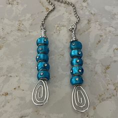 two blue beaded necklaces hanging from a silver chain on a marble counter top