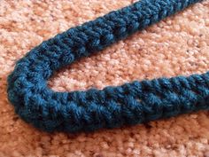 a blue crocheted object laying on top of a brown carpet next to a cell phone