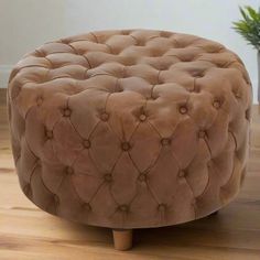 a round ottoman sitting on top of a wooden floor next to a potted plant