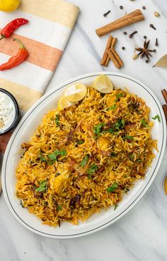 a white plate topped with yellow rice next to spices and lemons on a table