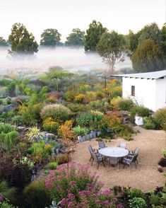 a table and chairs sitting in the middle of a garden with fog coming off the trees