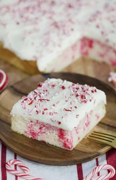 a piece of cake with white frosting and red sprinkles on a wooden plate