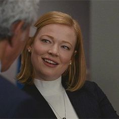 a woman smiling and talking to an older man who is wearing a black suit with white collar