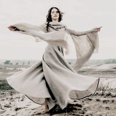 a woman in a long dress is standing on the sand with her arms spread out