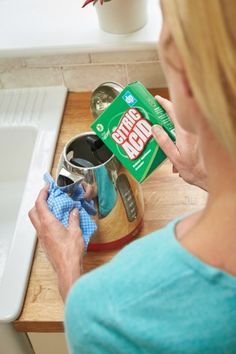 a woman cleaning the kitchen sink with dishwasher deterant and cloths in front of her