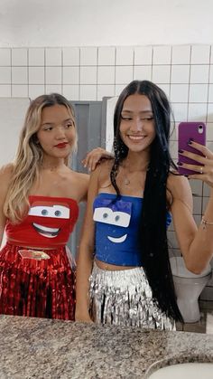 two women standing next to each other in front of a bathroom mirror holding up cell phones