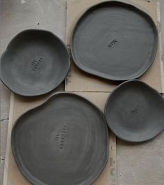 four gray plates sitting on top of a piece of cardboard next to each other with writing on them