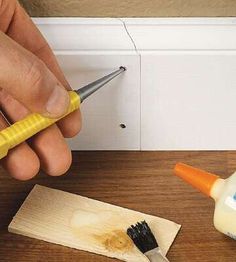 a person using a paint brush to fix a hole in the wall between two pieces of wood