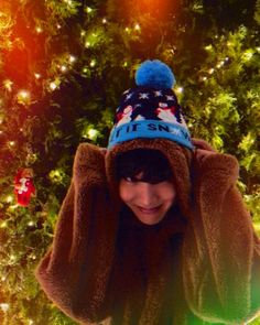 a young boy in front of a christmas tree wearing a blue and white knitted hat