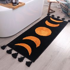 a black rug with orange circles and tassels on the floor next to a bathtub