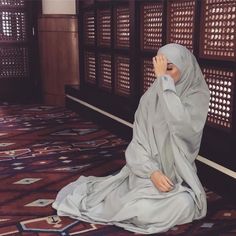 a statue of a woman sitting on top of a rug next to a wooden wall