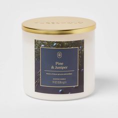 a white candle with gold lid and blue label on the top that says pine & jumper