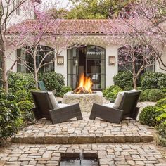 an outdoor fire pit with two chairs and a table in front of it, surrounded by trees