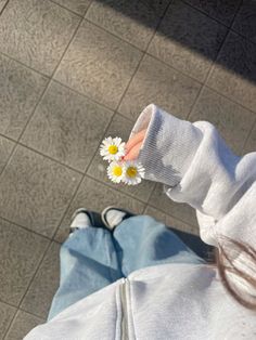 a person holding a daisy in their hand on the ground next to a tile floor