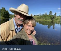 a man and woman taking a selfie in front of a lake with trees on the other side