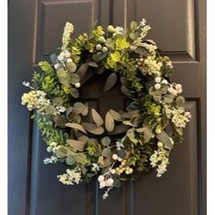 a wreath is hanging on the front door with greenery and white flowers in it