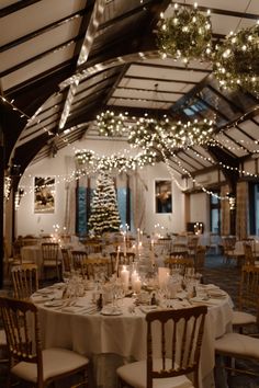 a dining room with tables and chairs covered in white tablecloths, lit by christmas lights