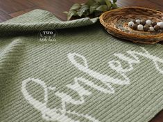 a green crocheted rug with the word welcome written on it next to a wicker basket