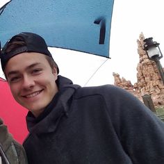 two people standing under an umbrella in front of a rock formation with a sky background