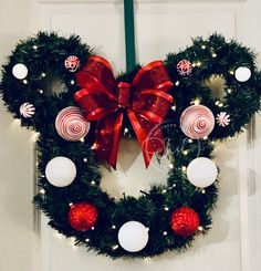 a mickey mouse wreath with red and white ornaments hanging on the front door for christmas