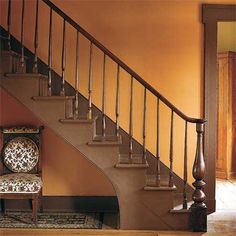 a chair sitting in front of a stair case next to a wooden floor and red wall