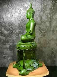 a green buddha statue sitting on top of a wooden table next to a gray wall