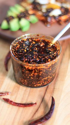 a glass filled with some kind of sauce on top of a wooden table next to red peppers