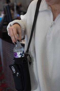 a woman is holding a water bottle in her hand while wearing a white sweater and black fanny bag