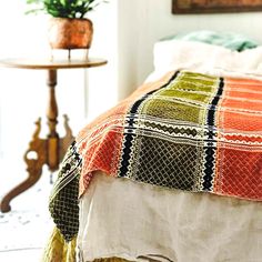 a bed with an orange, green and black quilt on it next to a small table