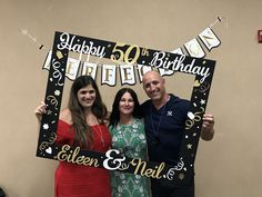 two women and a man pose for a photo in front of a sign that says happy birthday