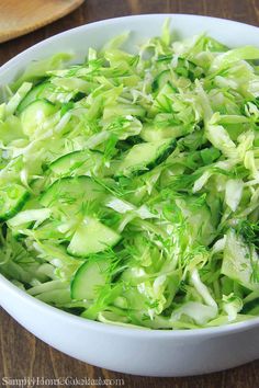 a white bowl filled with lettuce on top of a wooden table