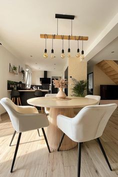 a dining room table with white chairs and a vase on top of it in front of stairs