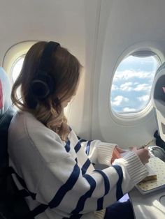 a woman sitting in an airplane with headphones on and looking at her laptop computer