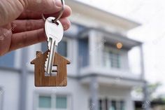 a hand holding a house key in front of a large white building with two story windows