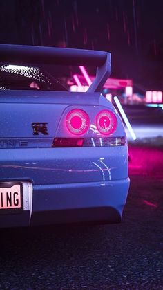 the back end of a blue car with its lights on in the rain at night