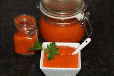 a small white bowl filled with sauce next to a large glass jar full of tomato sauce