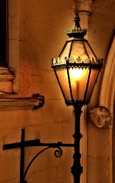 an old fashioned street light in front of a building with a cross on the wall