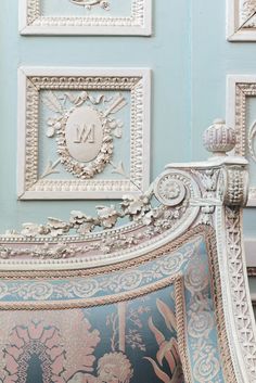 an ornately decorated bed frame in front of blue wall with framed pictures on it