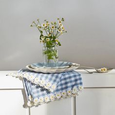 a vase with daisies on a table next to a blue and white napkins