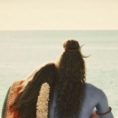 two women are sitting on the beach facing the ocean with their backs to each other