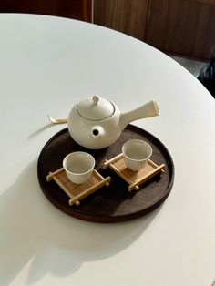 a white tea pot and two cups on a wooden tray