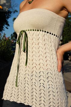 a woman wearing a white knitted top with a green tie around her waist