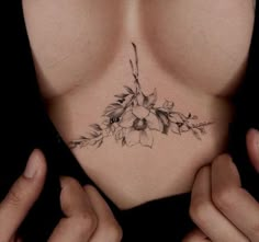 a woman's chest with flowers and leaves tattooed on her chest, behind her are two hands