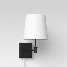 a black wall light with a white shade on it's head and plugged in